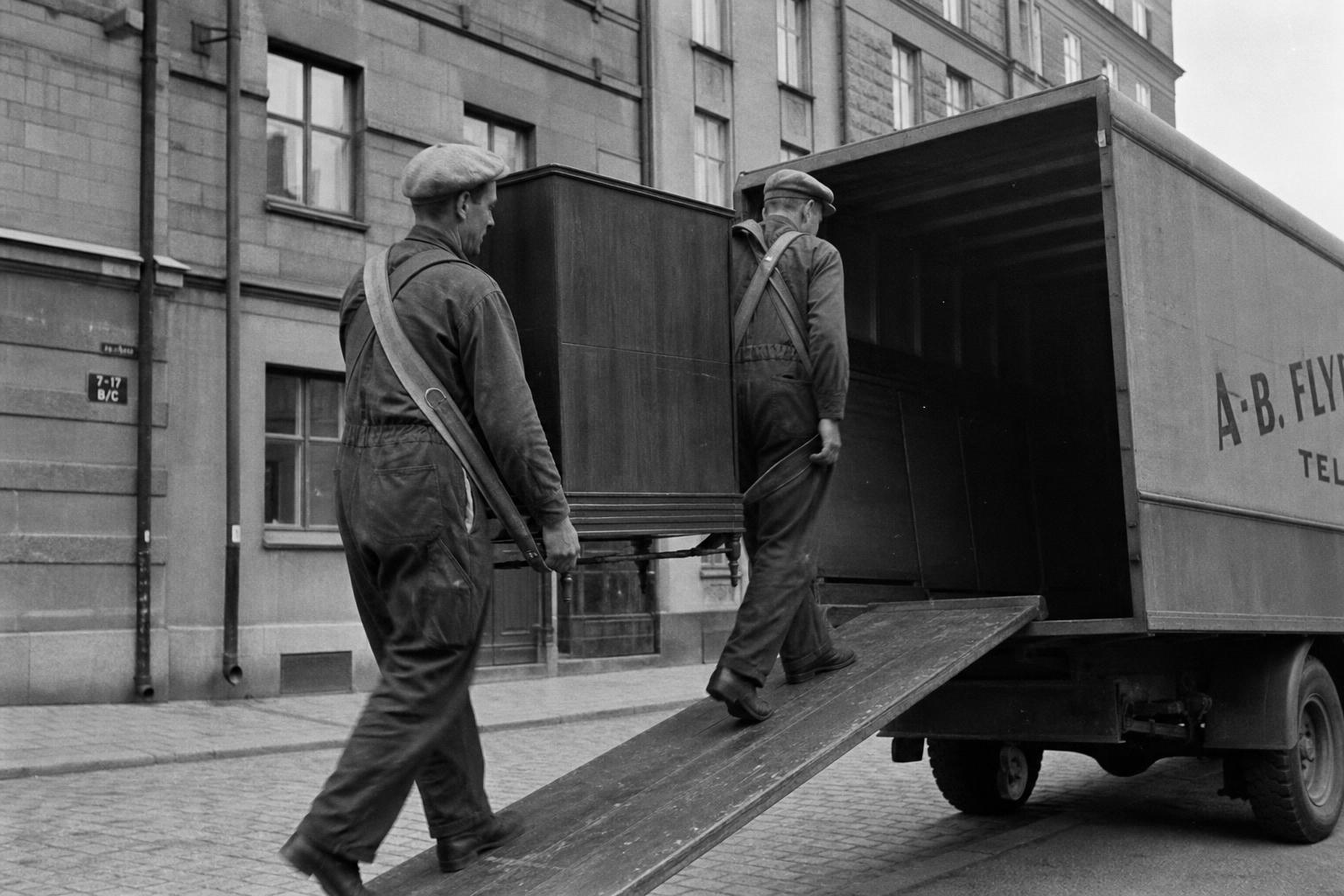 Flyttgubbar lastar en flyttbil från 1950-talet på en kullerstensgata i Norrland